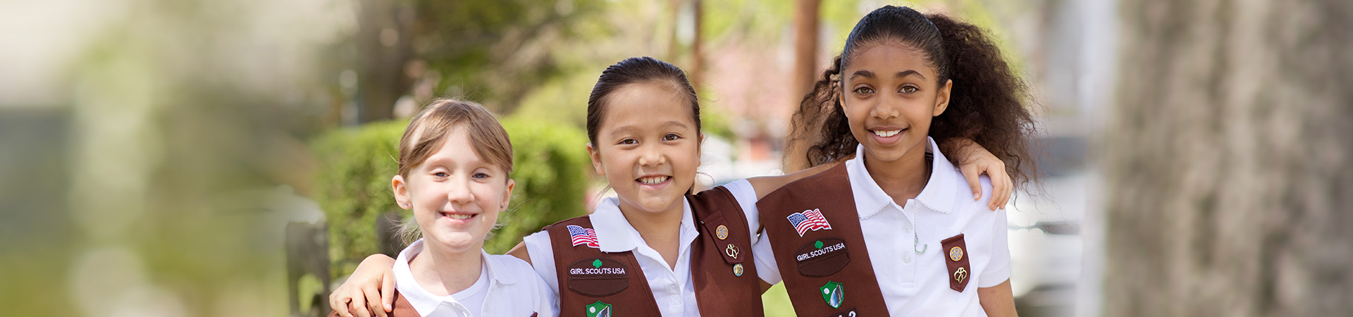  two girl scouts wearing trefoil clothing leaning on one another indoors 